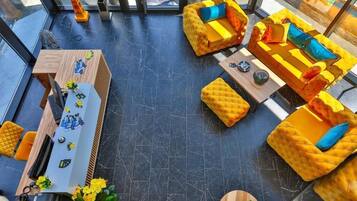 Un interior moderno con piso de mármol negro, sofás tapizados en amarillo con cojines azules, un escritorio de madera con una computadora y objetos decorativos, y una pared divisoria de vidrio con vista al exterior.