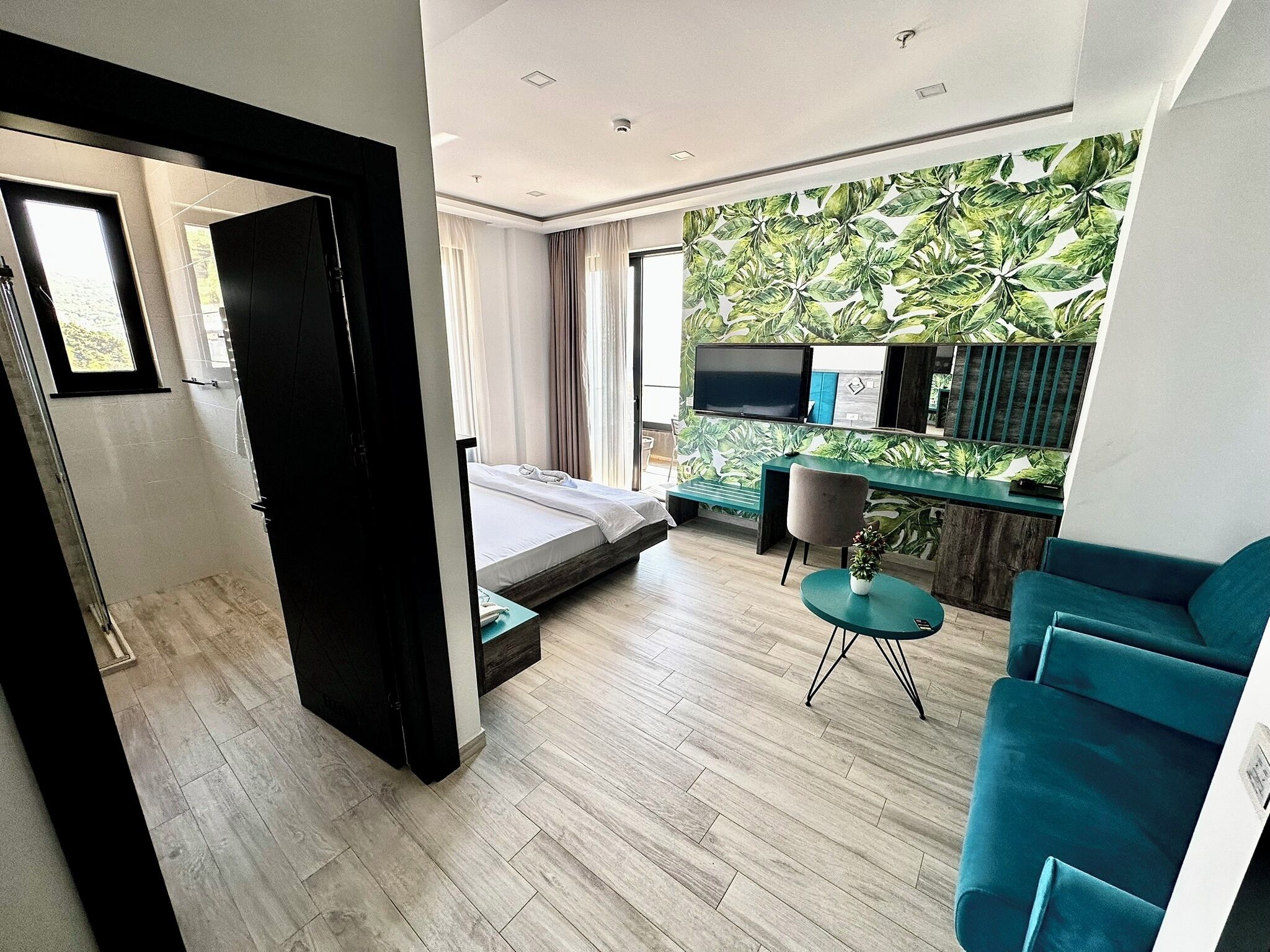 A modern hotel room with a bed, a desk, a TV, and a view of the outdoors.