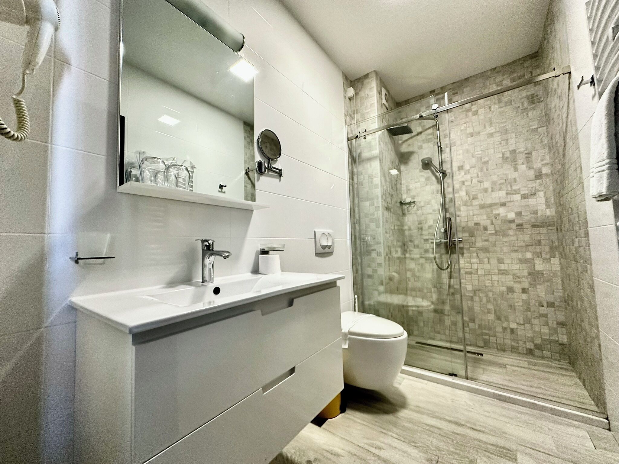 A modern bathroom with a glass-enclosed shower, a white sink with a mirror above, and a toilet.
