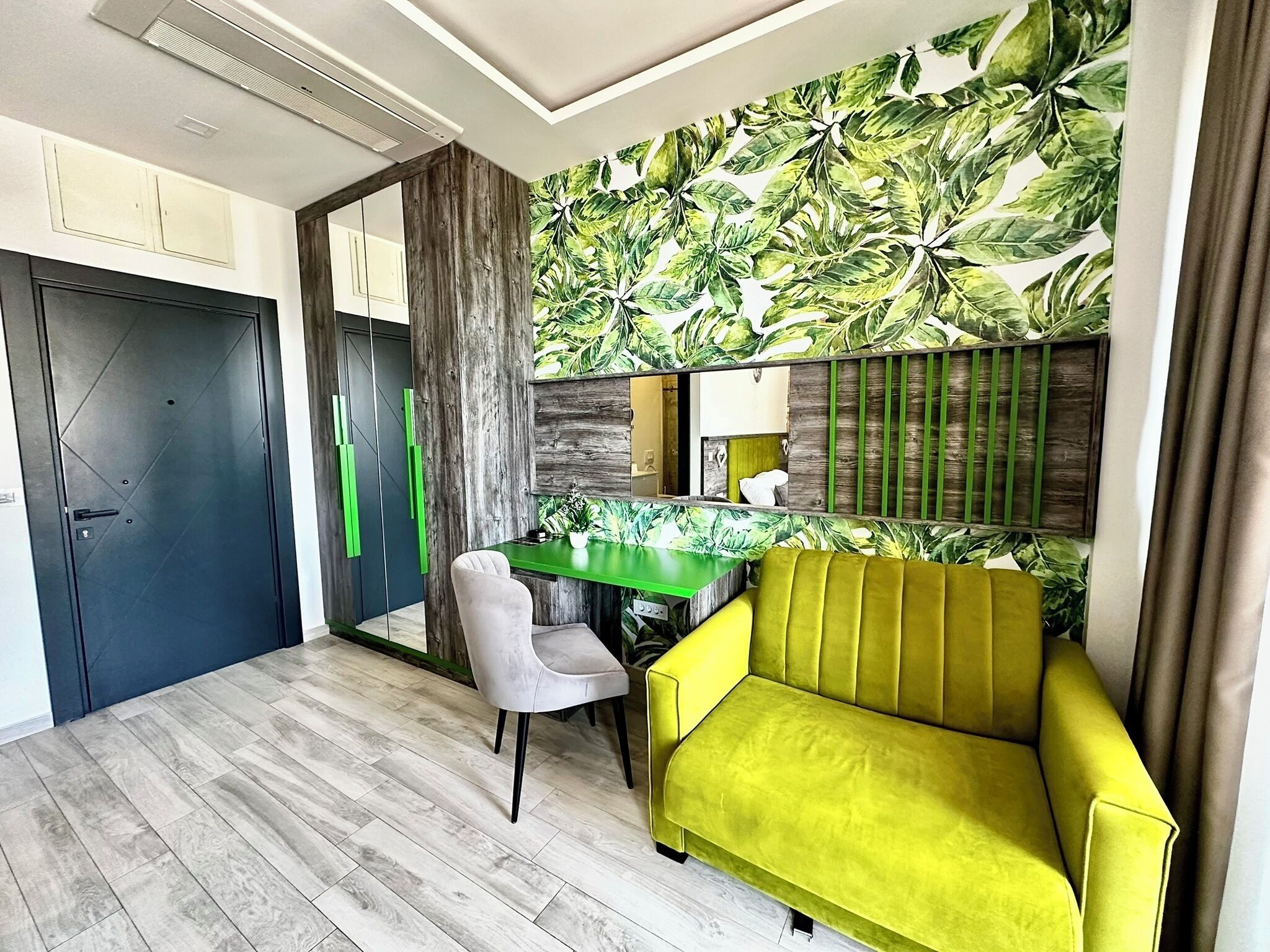 A modern room with a green desk, a yellow sofa, and a large mirror.
