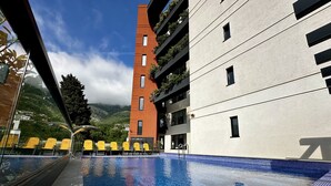 A modern hotel with a swimming pool, a mountain view, and a mix of red and grey building facades. - Hotel Del Medio (Sutomore)