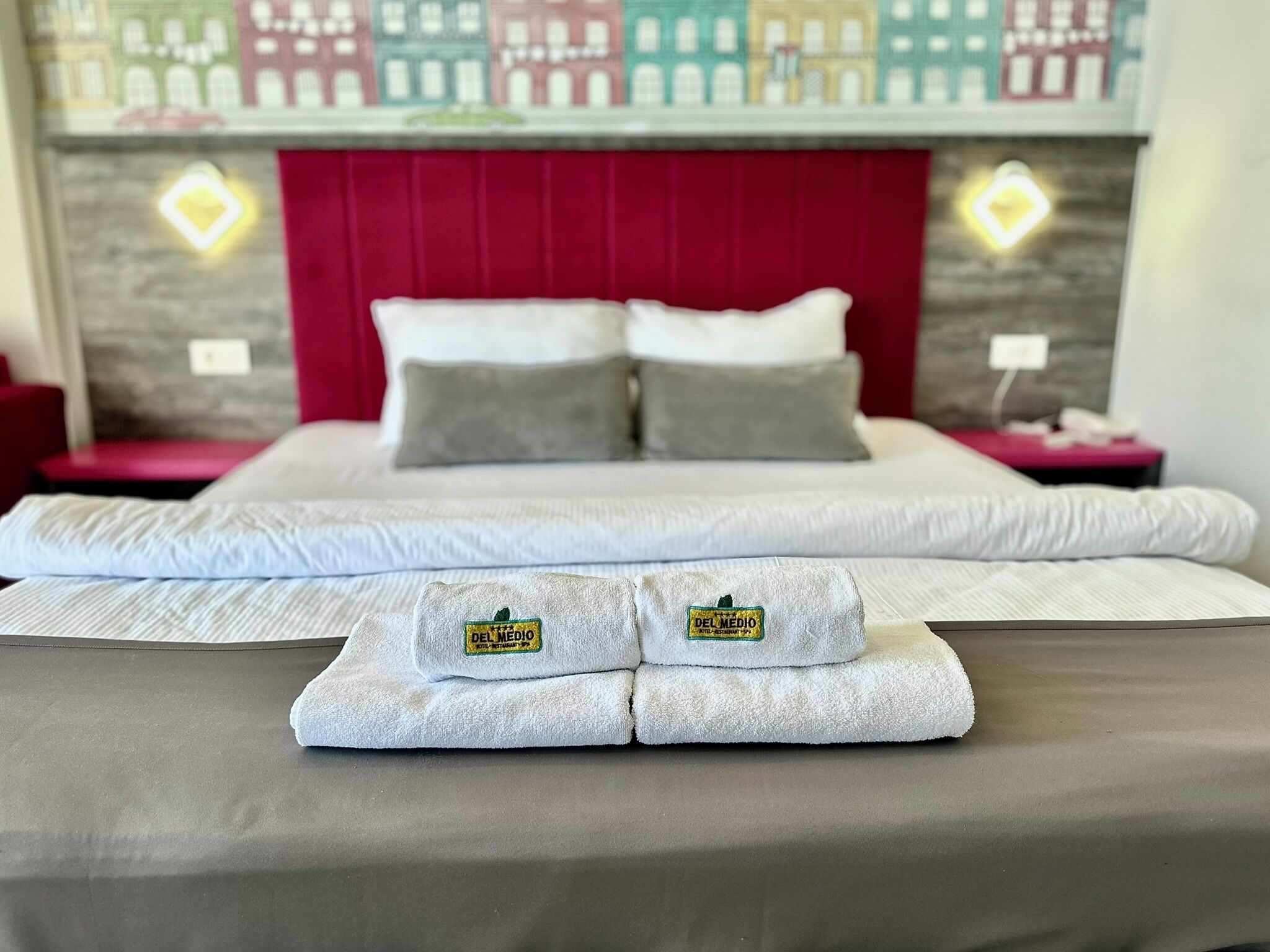 Una cama bien hecha con dos almohadas, un cabecero rojo y dos mesitas de noche con lámparas.