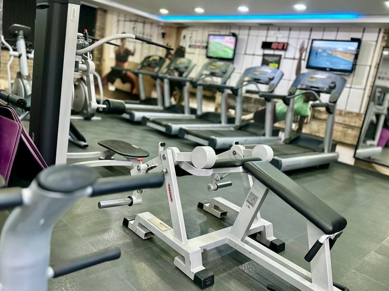 Un gimnasio con varias máquinas de ejercicio, incluyendo cintas de correr y equipo de levantamiento de pesas, dispuestas en filas.