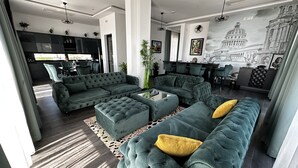 A modern living room with a sectional sofa, ottomans, and a dining area with bar stools. - Hotel Del Medio (Sutomore)