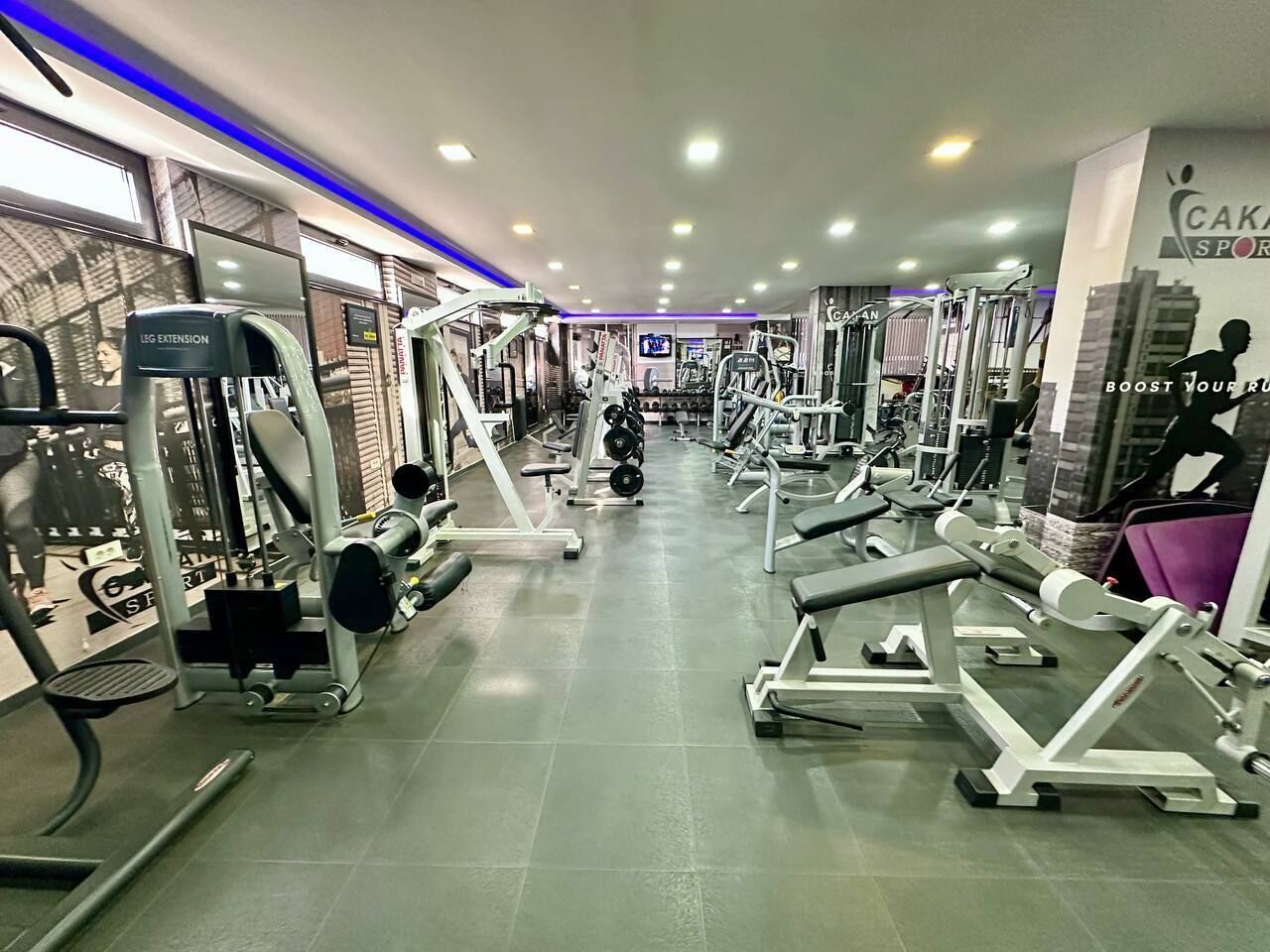 Un gimnasio con diferentes máquinas de ejercicio, pesas y una pantalla de televisión.