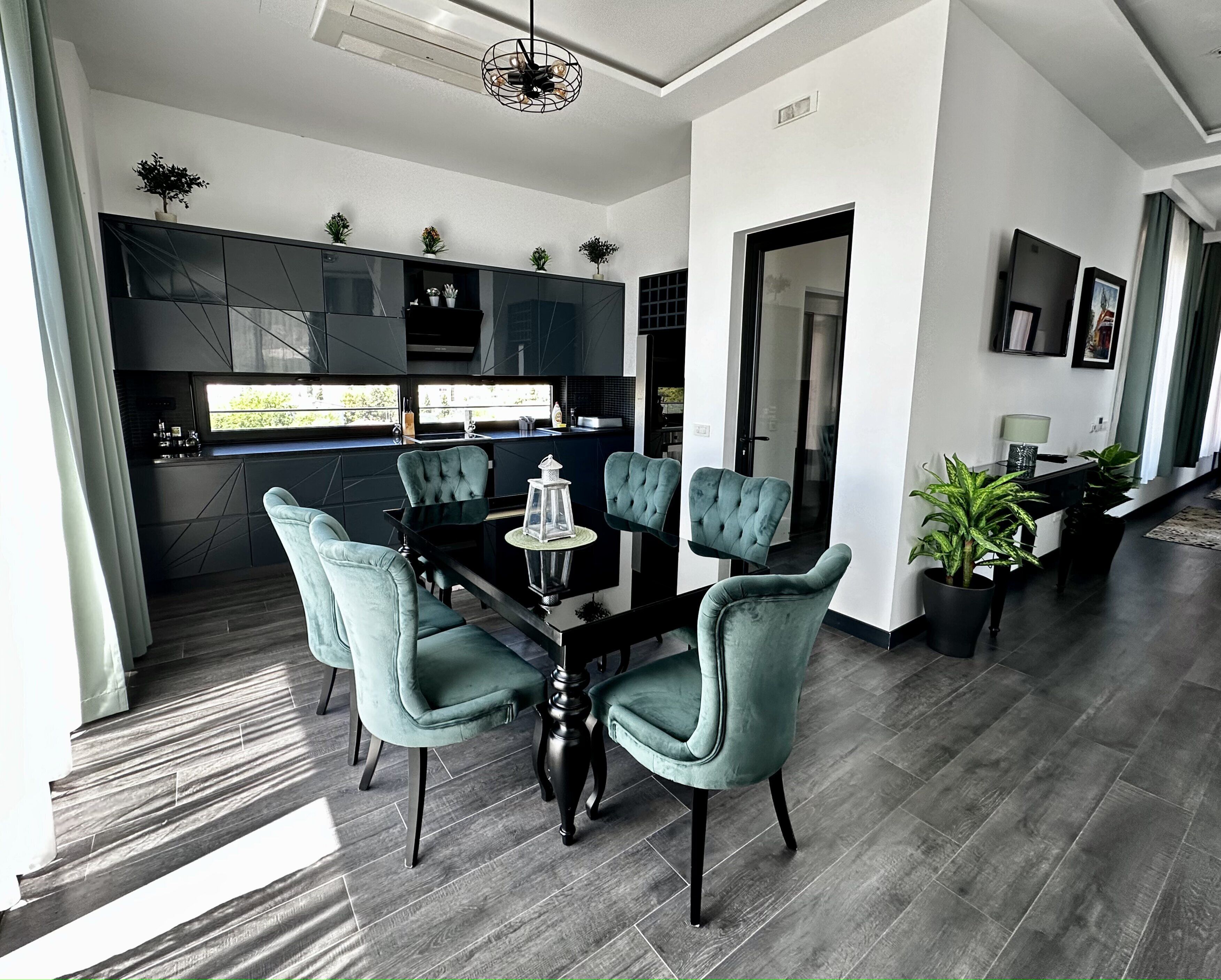 A modern dining area with a glass-top table, teal upholstered chairs, and a black chandelier.