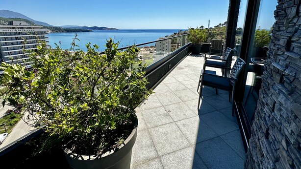 A balcony with a potted plant, outdoor seating, and a view of the sea and mountains. - Hotel Del Medio (Sutomore)