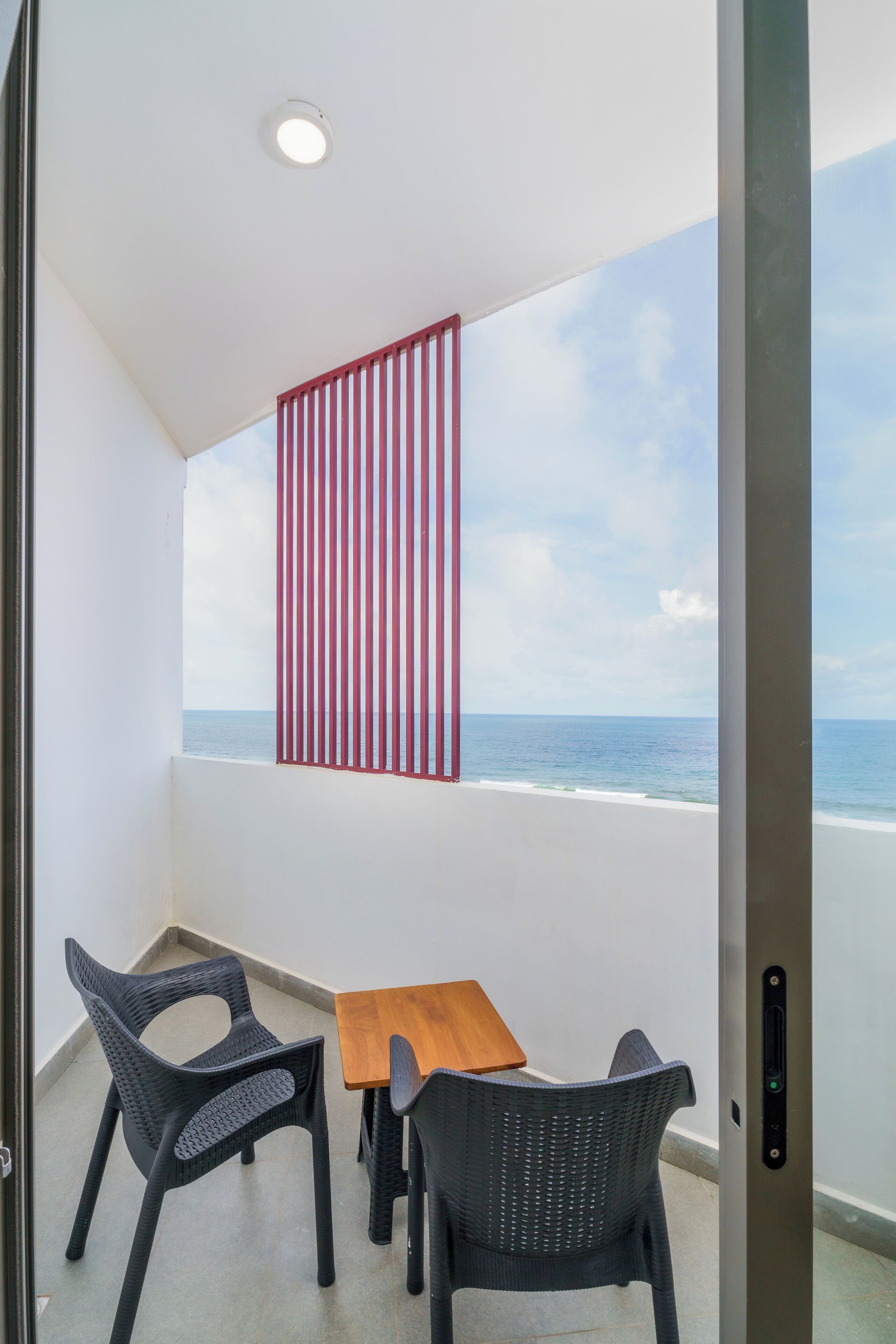 A balcony with a view of the sea, a wooden table, and two wicker chairs.