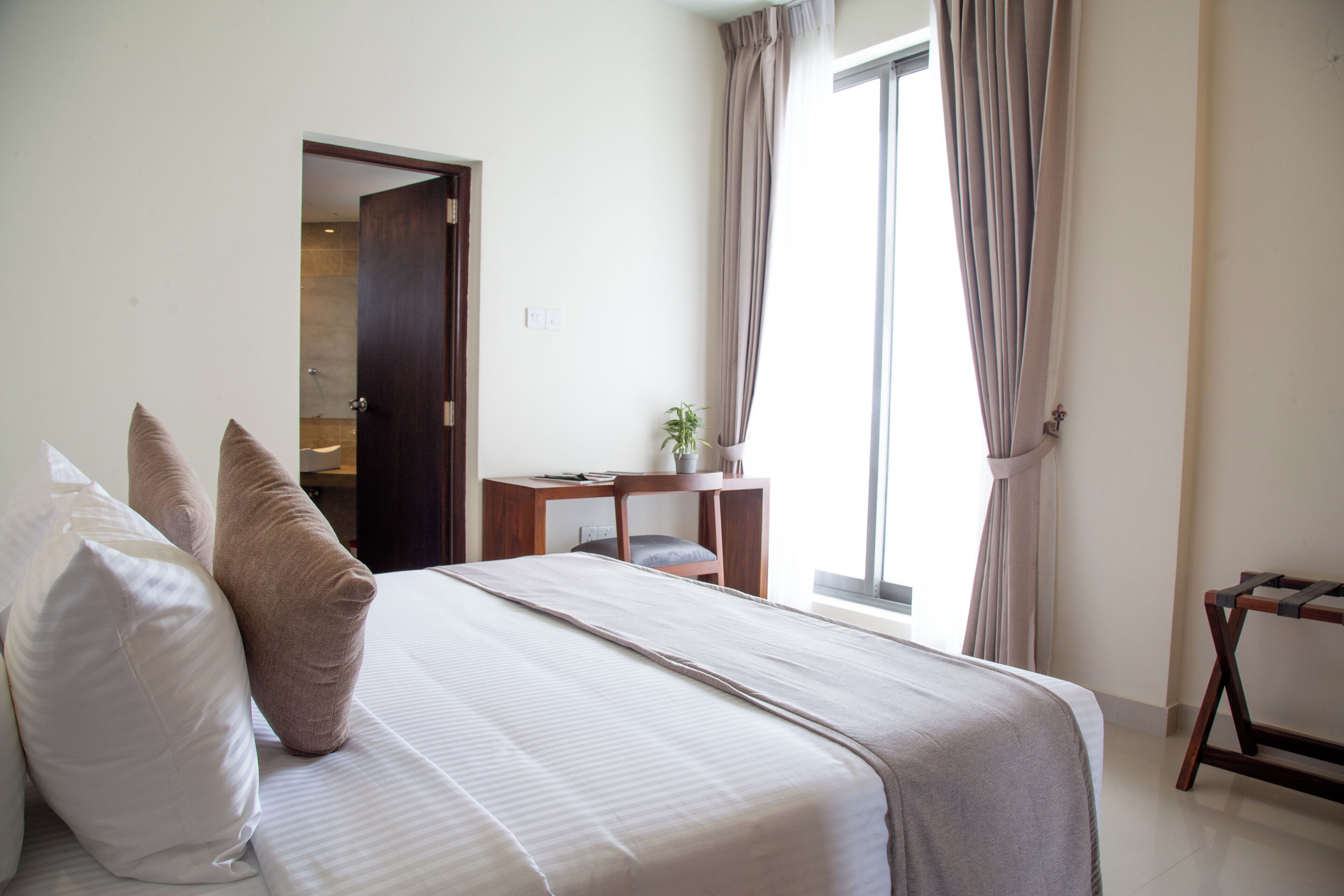 A hotel room with a bed, pillows, a desk, a chair, and a window with curtains.