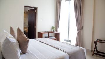 A hotel room with a bed, pillows, a desk, a chair, and a window with curtains.