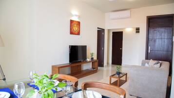 A modern living room with a sofa, a TV, and a dining table set for two.