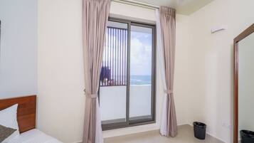 A hotel room with a large sliding glass door to the balcony, a bed with white bedding, and a small trash bin.