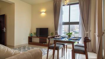 A living room with a sofa, a dining table set for four, a TV, and a window with curtains.