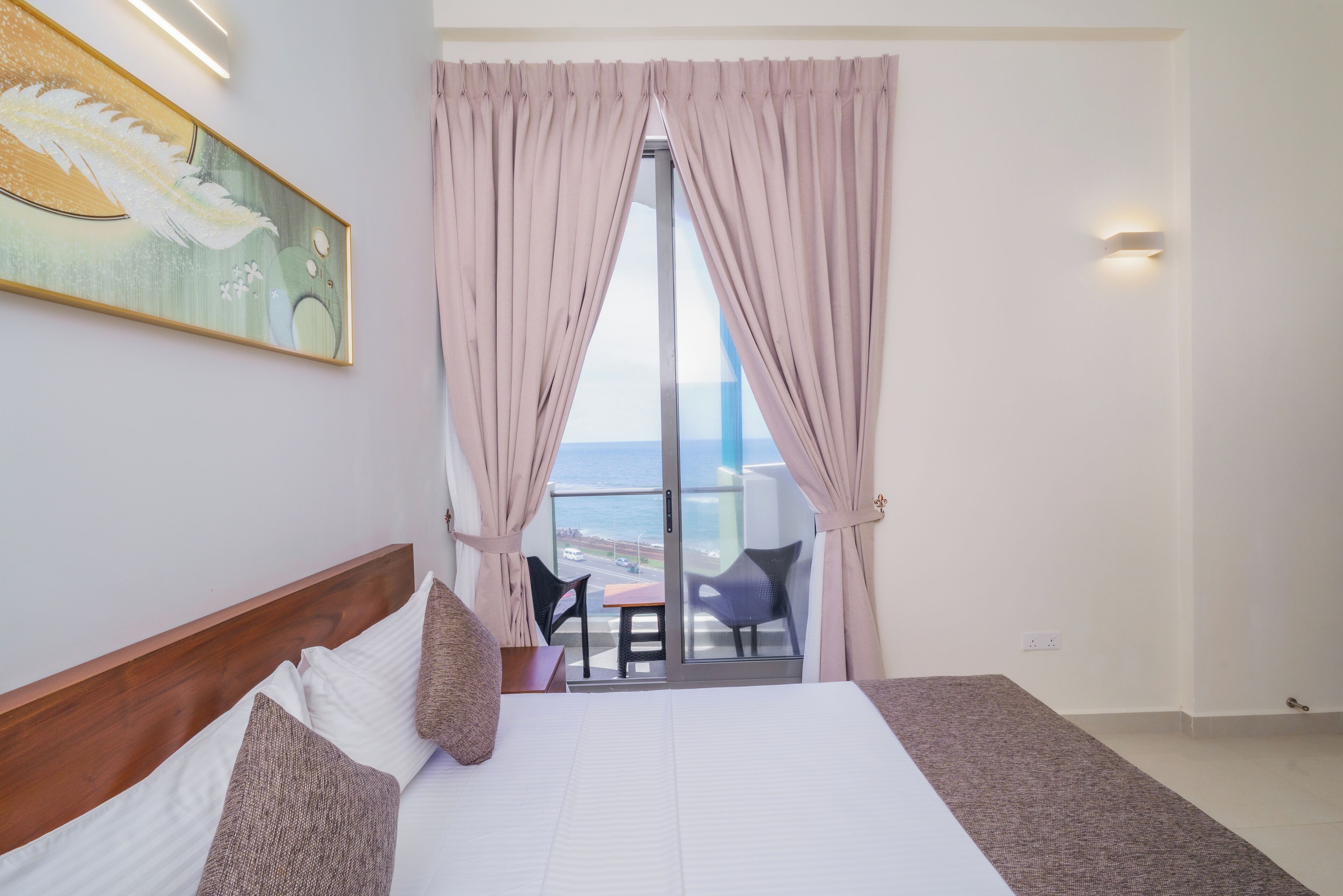 A hotel room with a large bed, a painting on the wall, and a balcony with a view.