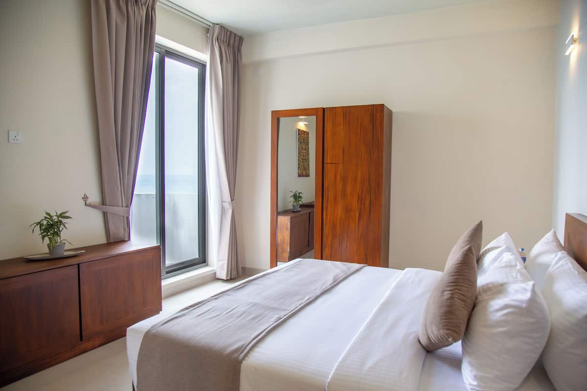 Quarto com cama, guarda-roupa de madeira, janela com cortinas e uma pequena planta no aparador.