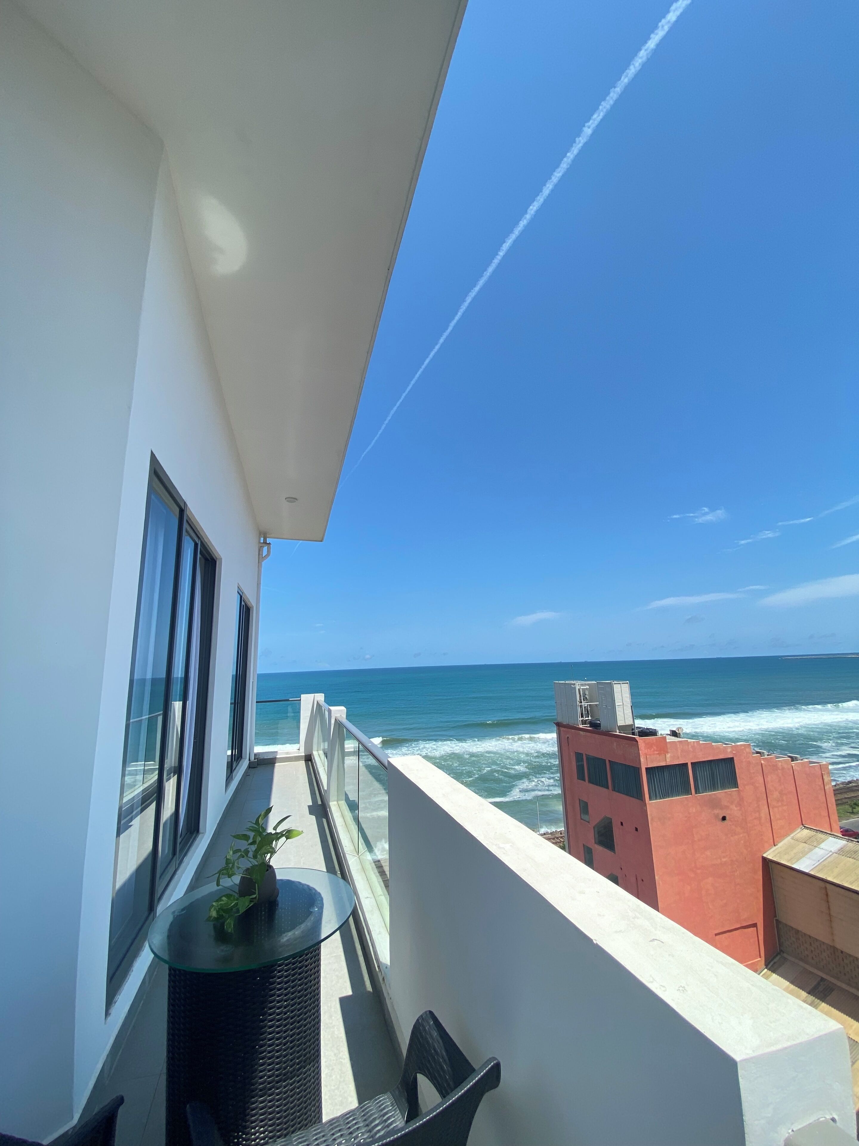 A balcony with a view of the ocean, a glass table, and a chair.
