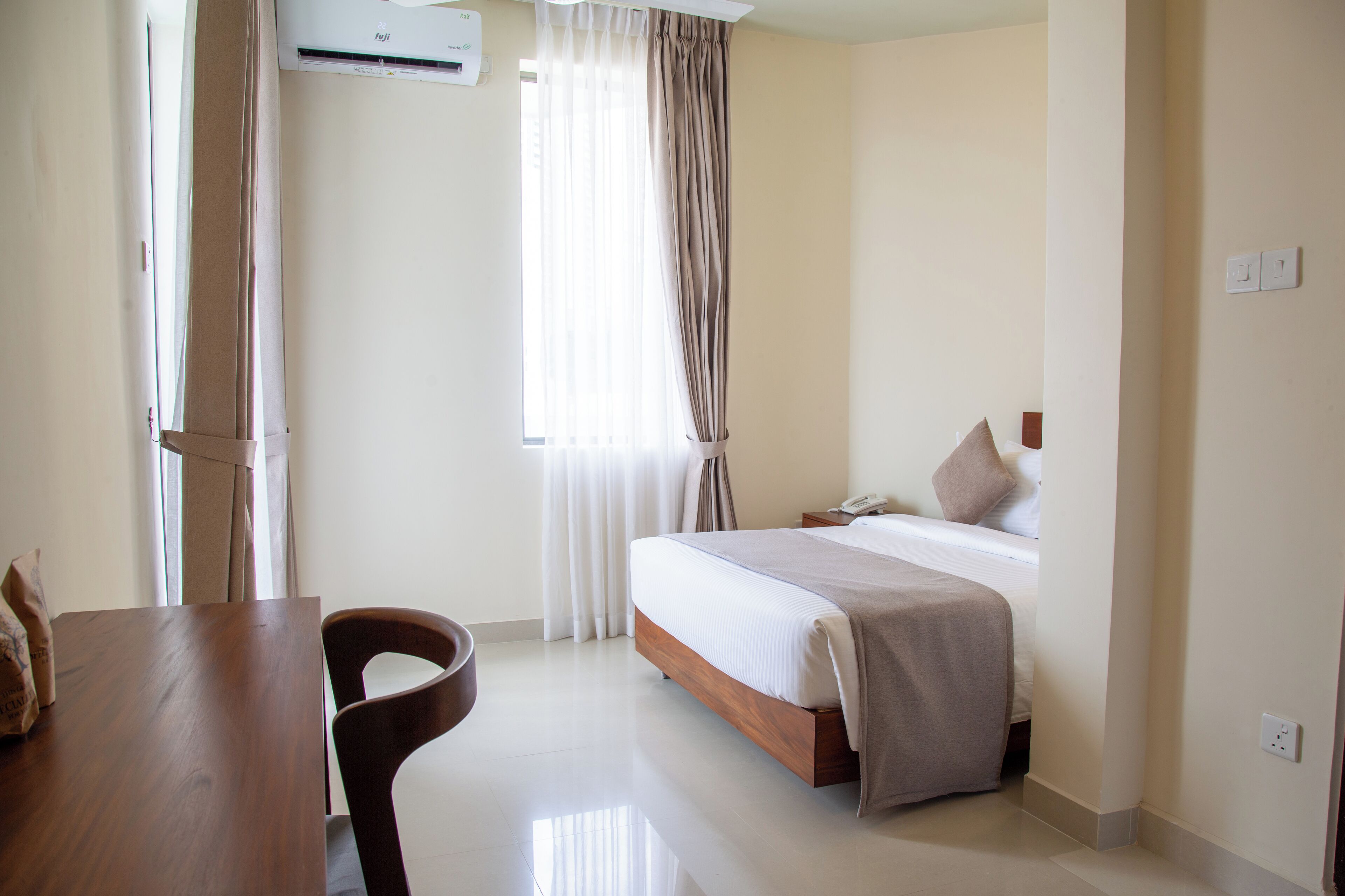 Quarto de hotel com cama, mesa de madeira, uma cadeira e janela com cortinas.