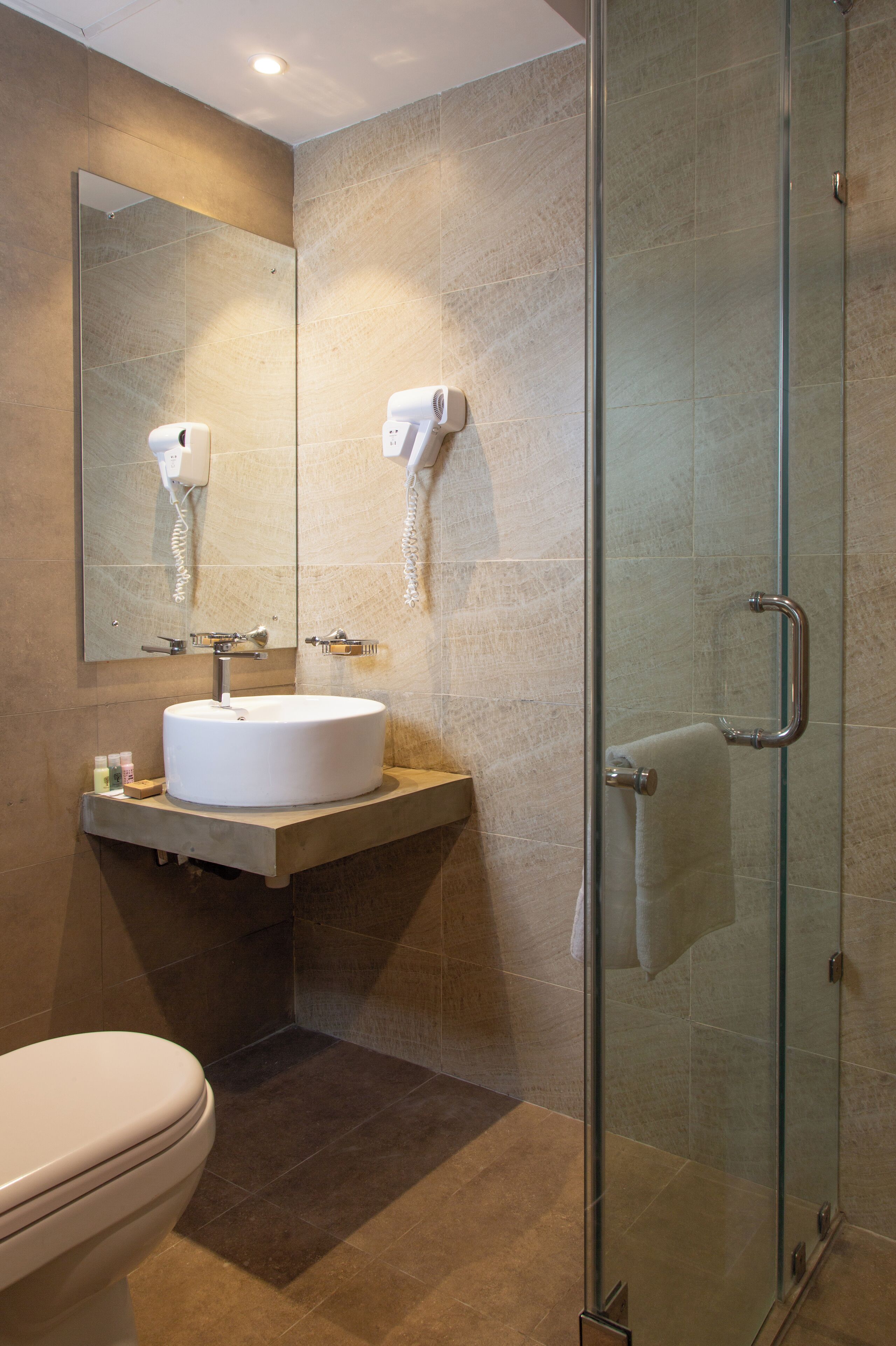 Une salle de bain avec un lavabo rond, des toilettes, une cabine de douche en verre et un miroir au-dessus du lavabo.