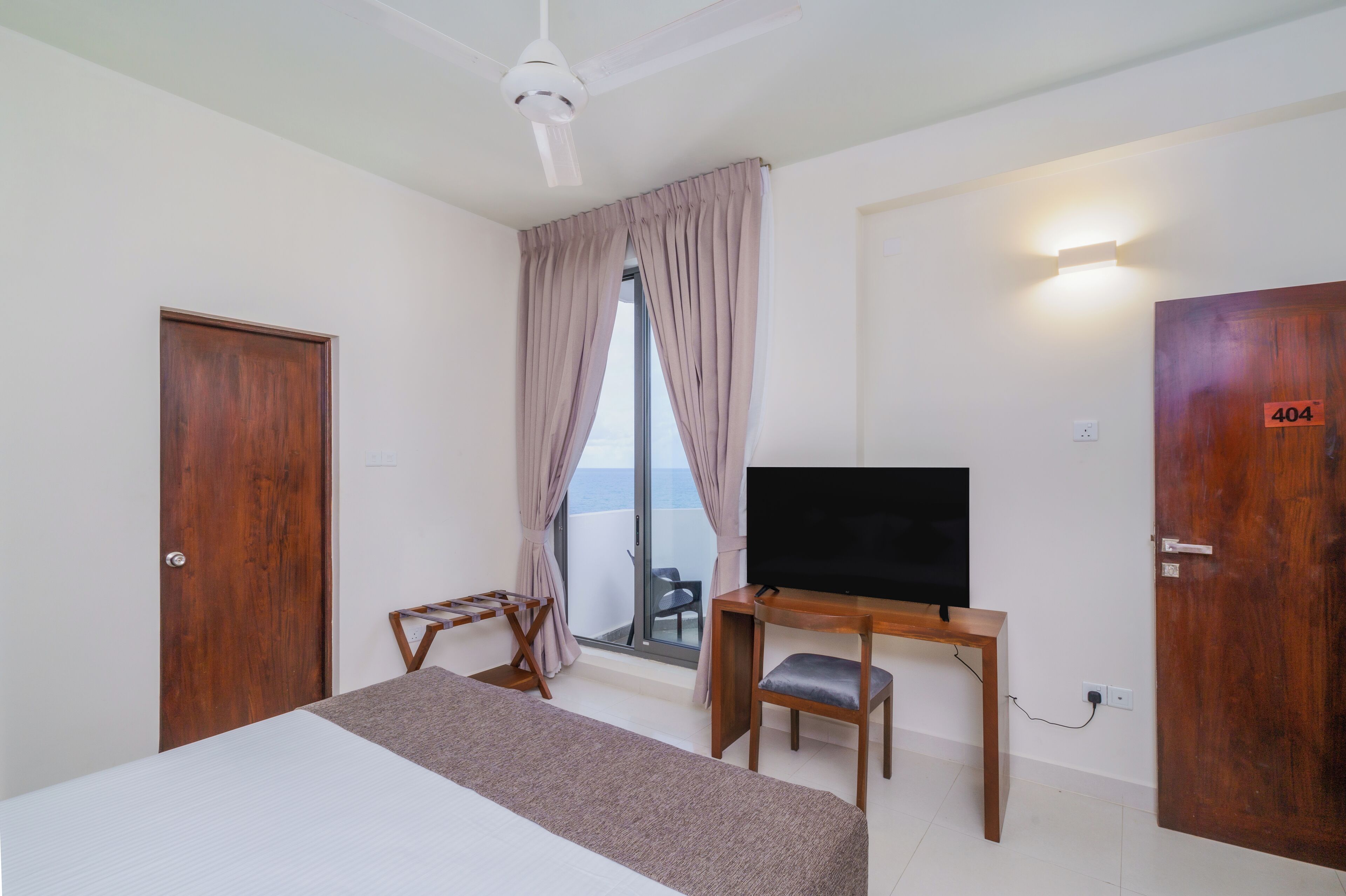 A hotel room with a bed, a desk with a chair, a television, and a balcony with a view.