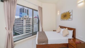 Habitación de hotel con un ventanal grande, una cama con cabecera de madera, una mesita de noche y una lámpara fijada a la pared.