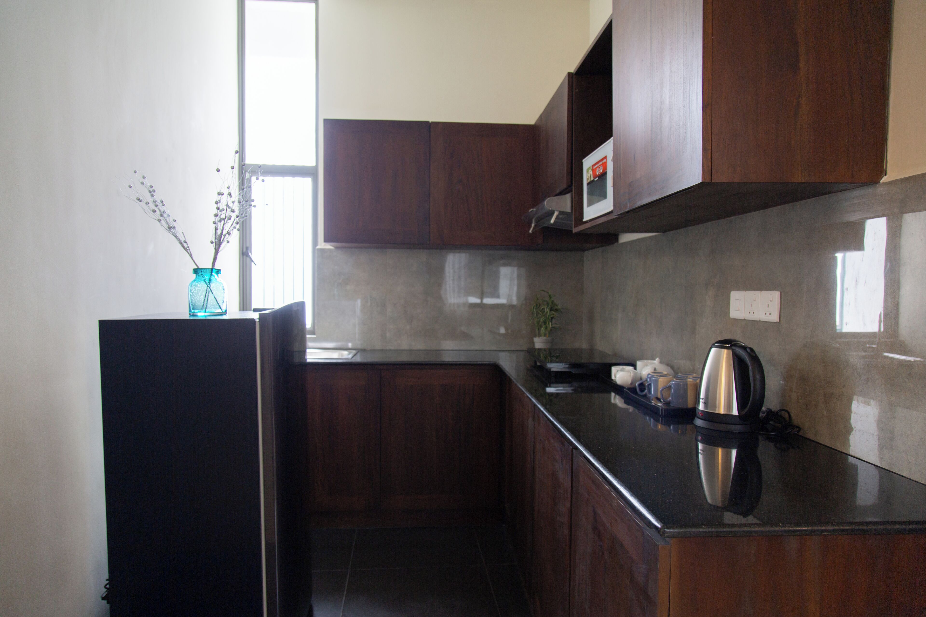 Cozinha moderna com armários de madeira escura, bancada preta e chaleira de aço inoxidável.
