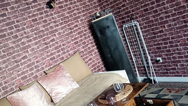 A room with a brick wall, a sofa with cushions, a wooden coffee table with wine glasses, and a radiator. - Studio Neuf à Maillane (Maillane)