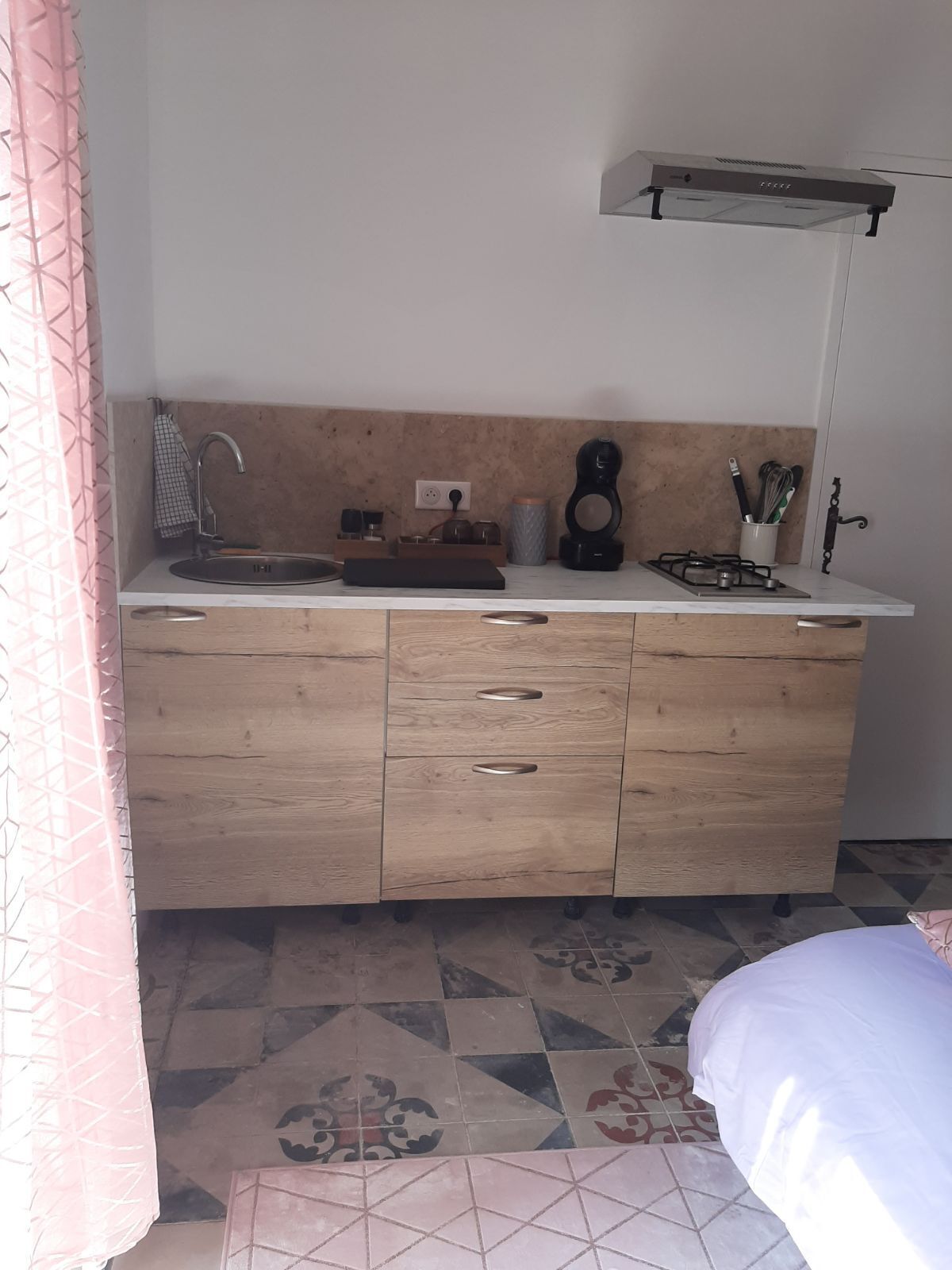 A small kitchenette with a sink, countertop, and a gas stove. There are cabinets below the countertop and a power outlet on the wall.