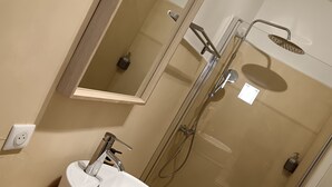 A bathroom with a white sink, a mirror, and a glass-enclosed shower. - Studio Neuf à Maillane (Maillane)
