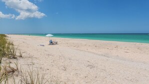 Une plage avec un ciel dégagé, quelques personnes et un petit parasol.