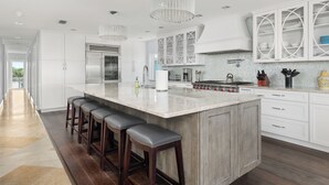 Une cuisine moderne dotée d’un grand îlot central, de tabourets de bar, de meubles blancs et de luminaires suspendus.