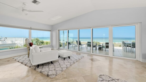 Un salon spacieux avec un canapé blanc, une table basse et une grande fenêtre donnant sur une plage.