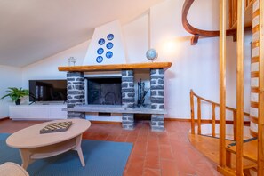 A living room with a stone fireplace, a television, and a wooden staircase. - Appartamento La Chiocciola by Wonderful Italy (Bellagio)