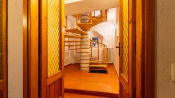Una escalera en espiral de madera en un pasillo con suelo de baldosas y una puerta con panel de vidrio.