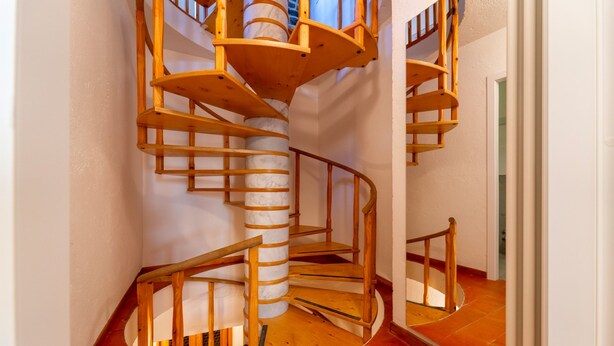 Una escalera en espiral de madera con un columnario de mármol en un pasillo.