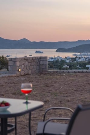 A coastal view with a stone wall, a table with a glass of red wine, and boats in the background. - Sea & Garden View Parasporos Houses, Adamas Milos (Milos)