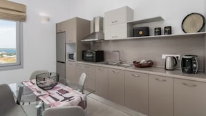 Cozinha moderna com eletrodomésticos embutidos, sala de jantar com mesa de vidro e vista pela janela.