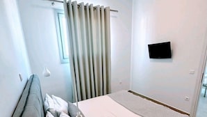 Quarto de hotel moderno com uma cama de solteiro, televisão de tela plana na parede e uma janela com cortinas.