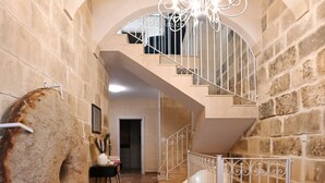 A stone-walled hallway with a large rock, a chandelier, and a staircase leading to an upper level. - A Unique and Charming Farmhouse with Heated Pool. (L-Gnasri)