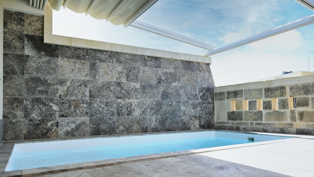 A swimming pool with a stone wall and a pergola overhead. - A Unique and Charming Farmhouse with Heated Pool. (L-Gnasri)