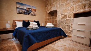 A bedroom with a stone wall, a bed with a blue bedspread, pillows, and neatly folded towels. - A Unique and Charming Farmhouse with Heated Pool. (L-Gnasri)