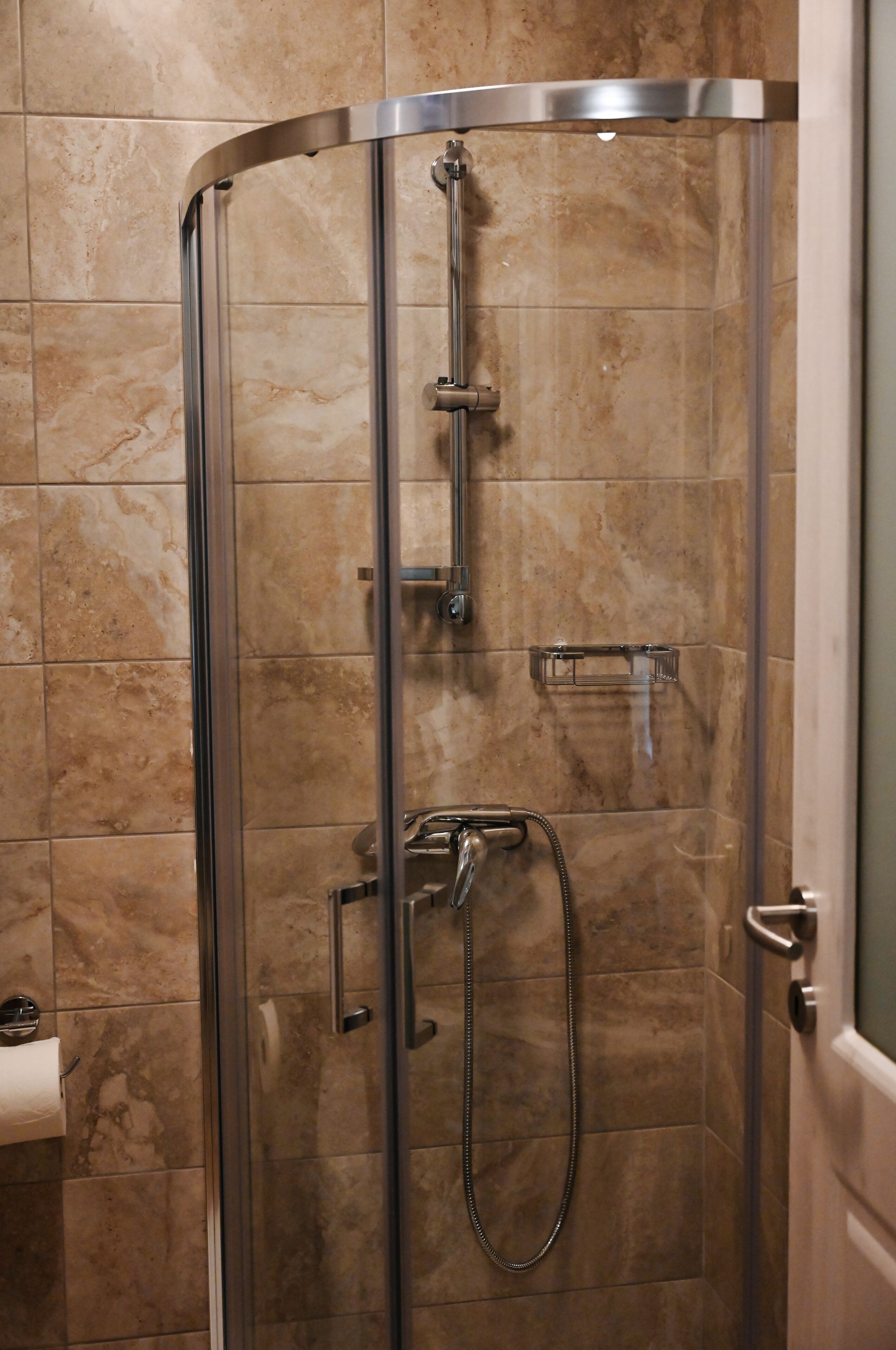 Une cabine de douche fermée par des parois en verre, équipée d’un pommeau de douche à main et d’un flexible de douche à main.