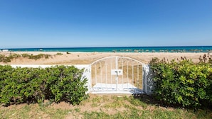 A beach view with a white gate leading to a pathway, surrounded by greenery.