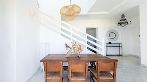A dining area with a wooden table and chairs, a woven pendant light, a staircase, and a round mirror on the wall.