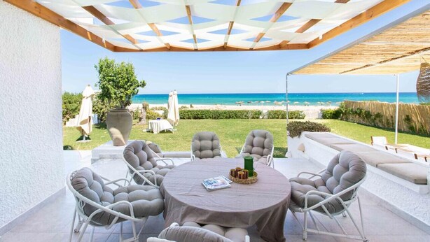 A patio with a round table and chairs, a view of the sea, and a pergola overhead.