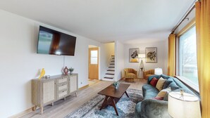 Ein modernes Wohnzimmer mit Flachbildfernseher, einer Holzkommode, einem Sofa, einem Couchtisch und einer Treppe zu einem anderen Raum.
