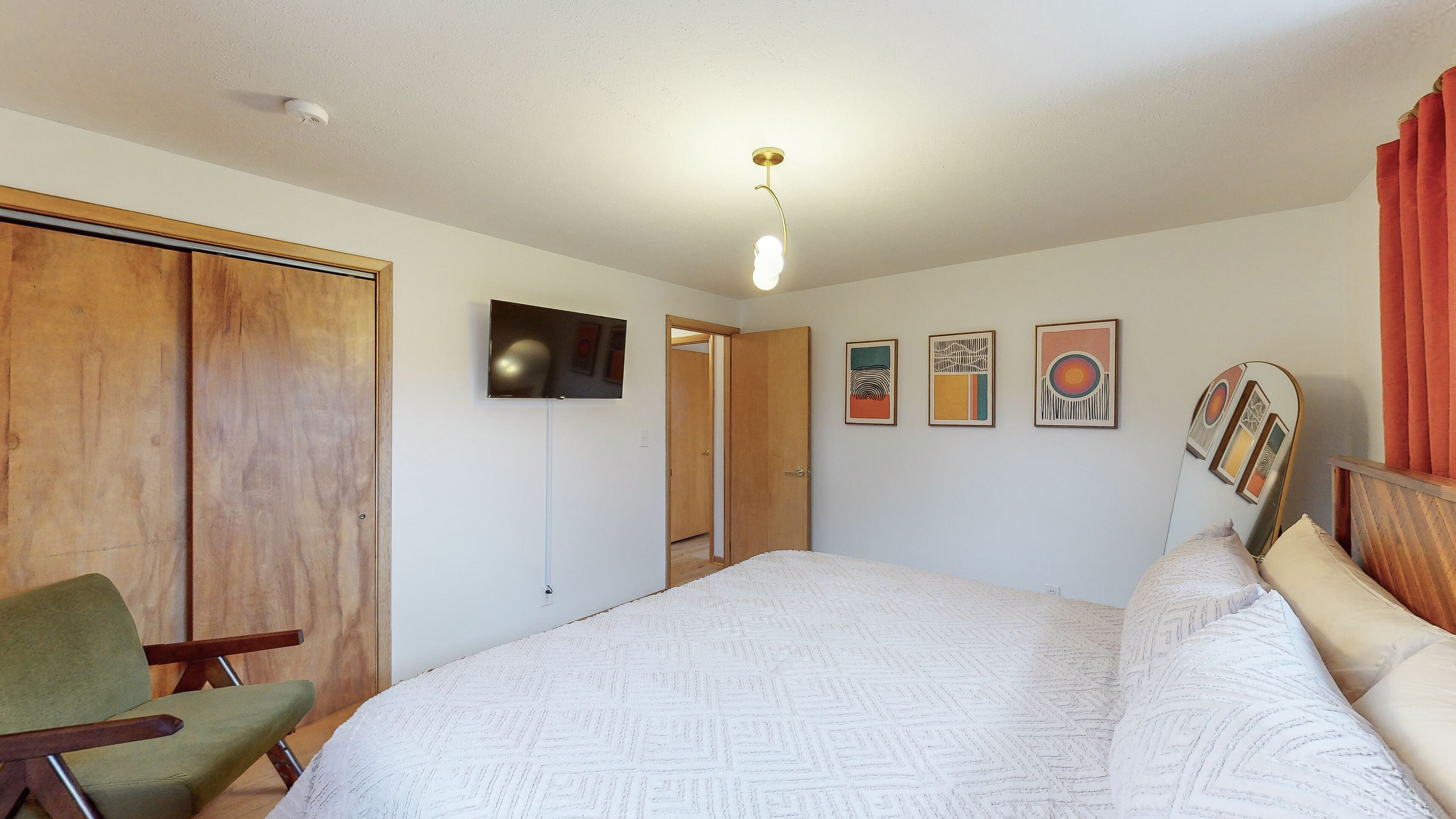 Une chambre à coucher avec un lit, une chaise, un téléviseur et des œuvres d’art accrochées au mur.