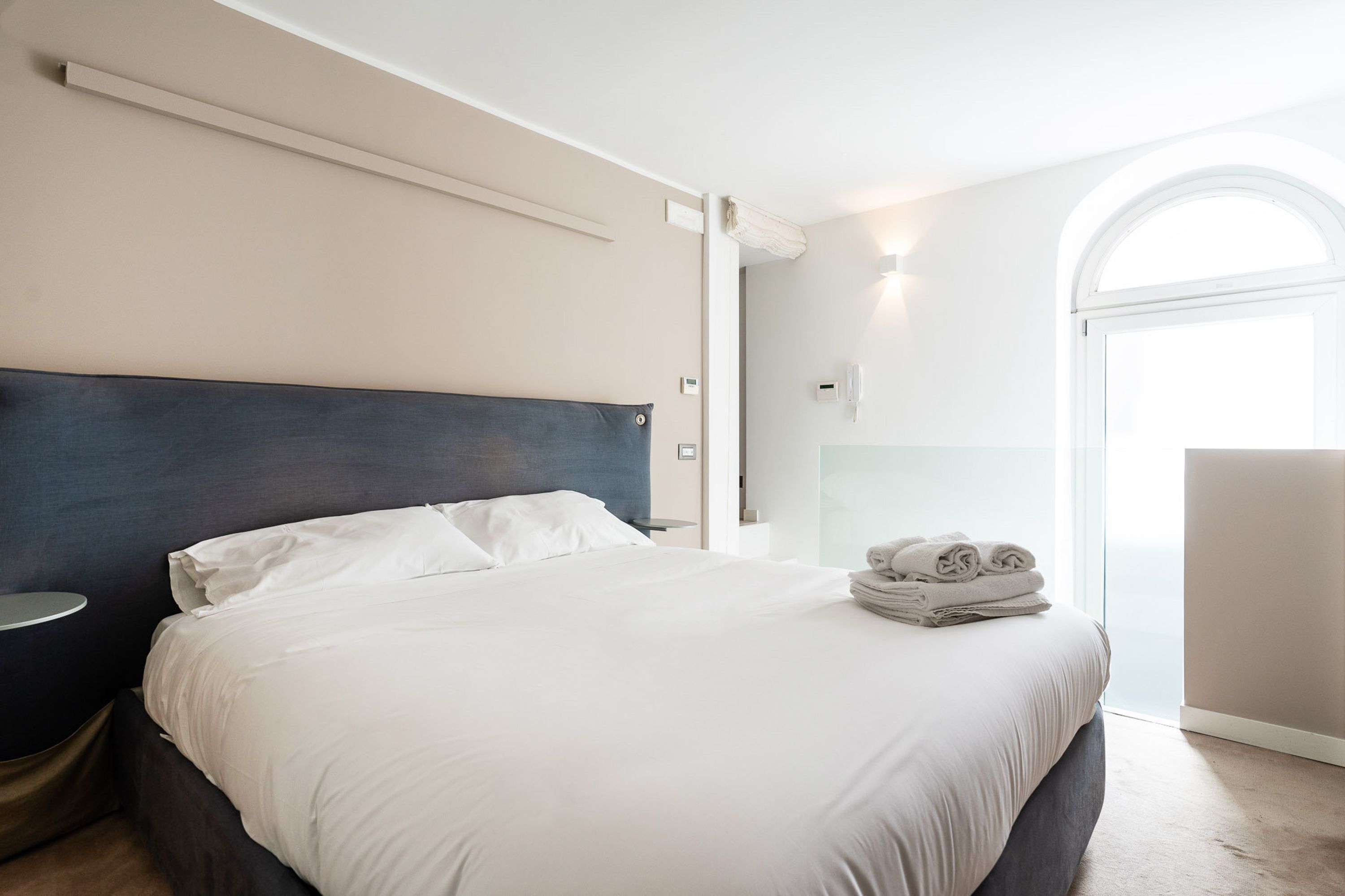 Een moderne hotelkamer met een groot bed, een nachtkastje en uitzicht op het omliggende landschap door een groot raam.