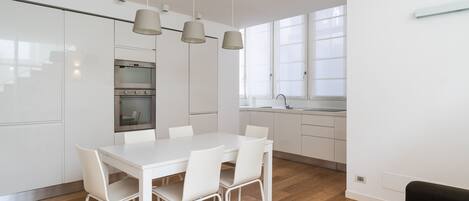 A modern kitchen with white cabinets, a built-in oven, and a dining area with a white table and chairs.
