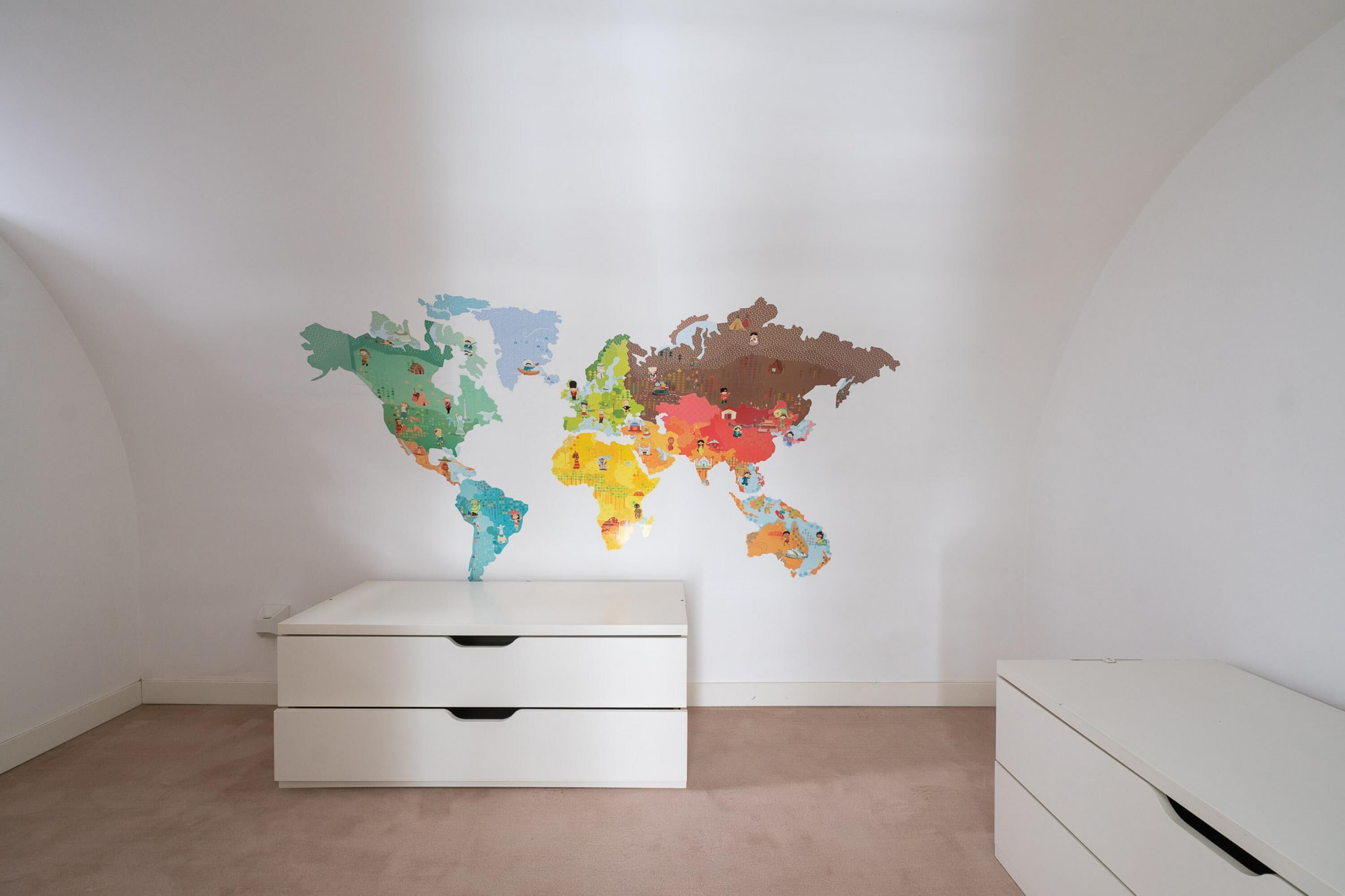 A room with a world map wall art, a white dresser, and a white cabinet.