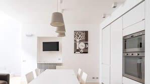 A modern kitchen with built-in appliances, a dining area with a white table and chairs, and a mounted TV.
